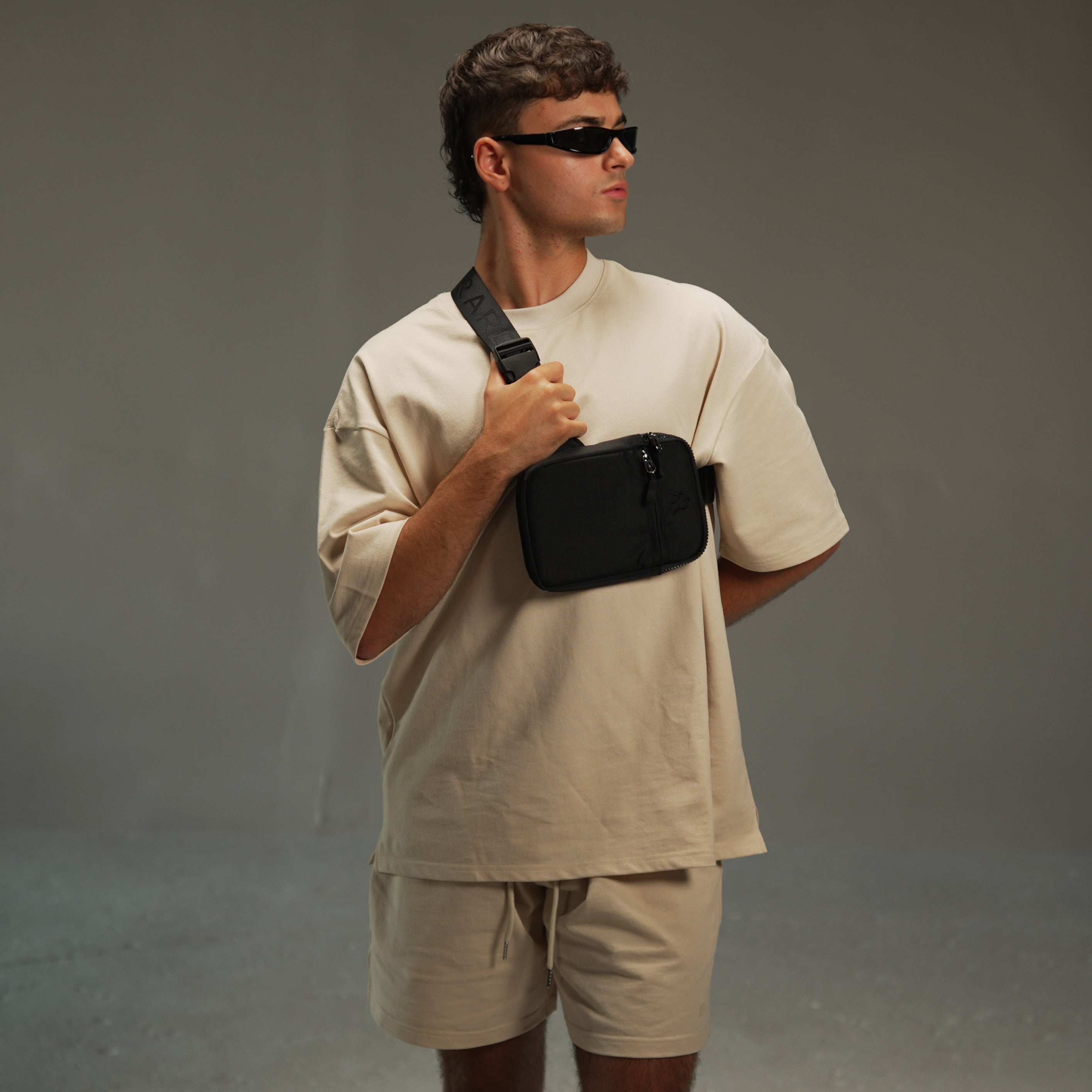 Male model wearing the iRARE black crossbody bag styled with neutral apparel in a studio setting