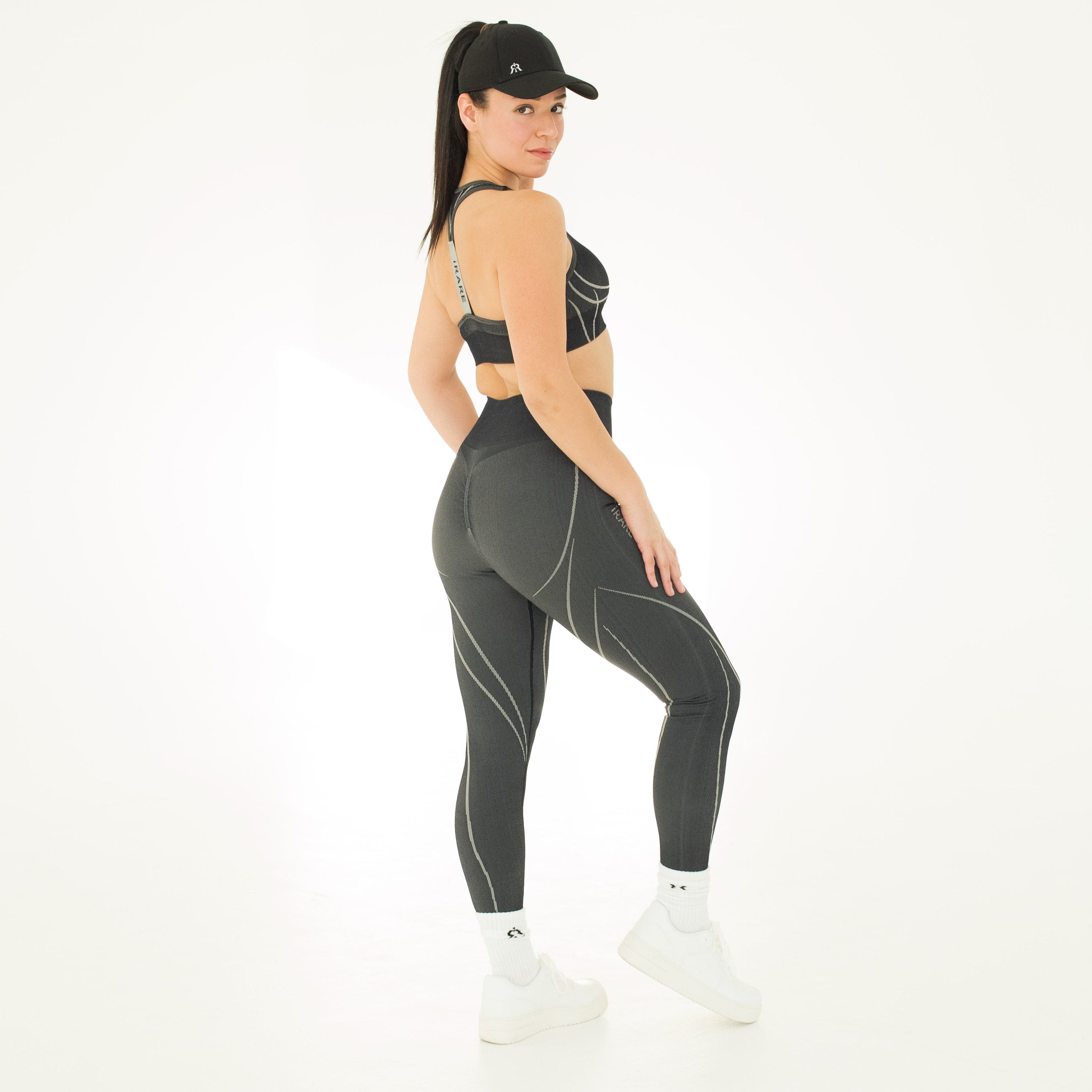 styled look with black seamless leggings, matching sport bra, and cap on studio backdrop