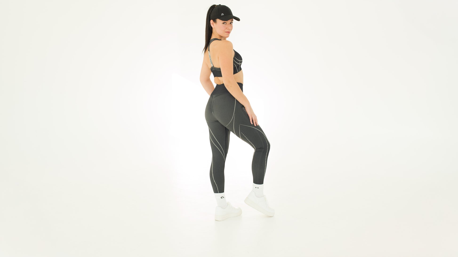 styled look with black seamless leggings, matching sport bra, and cap on studio backdrop